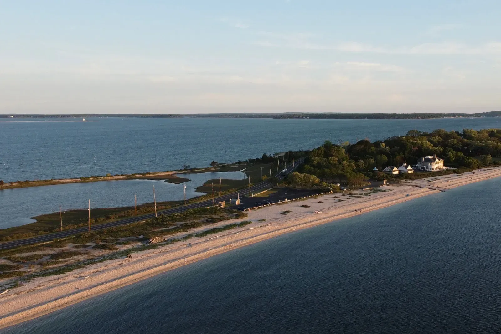 Aerial view of a beach, a road and salt marsh along a calm bay at sunset