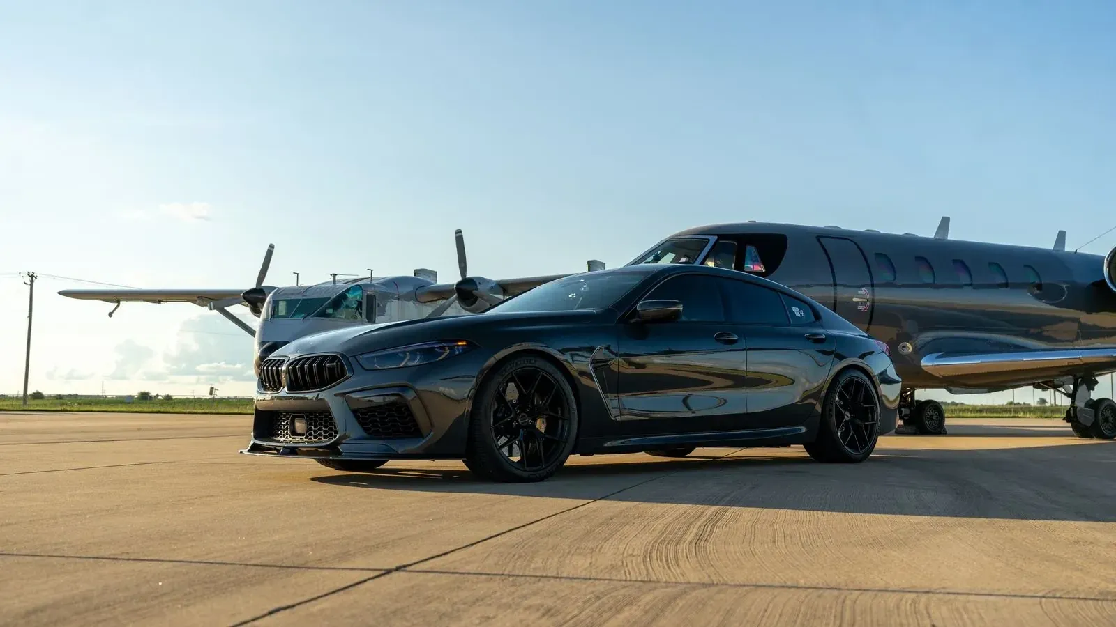 A black car parked beside a private jet on an airport apron