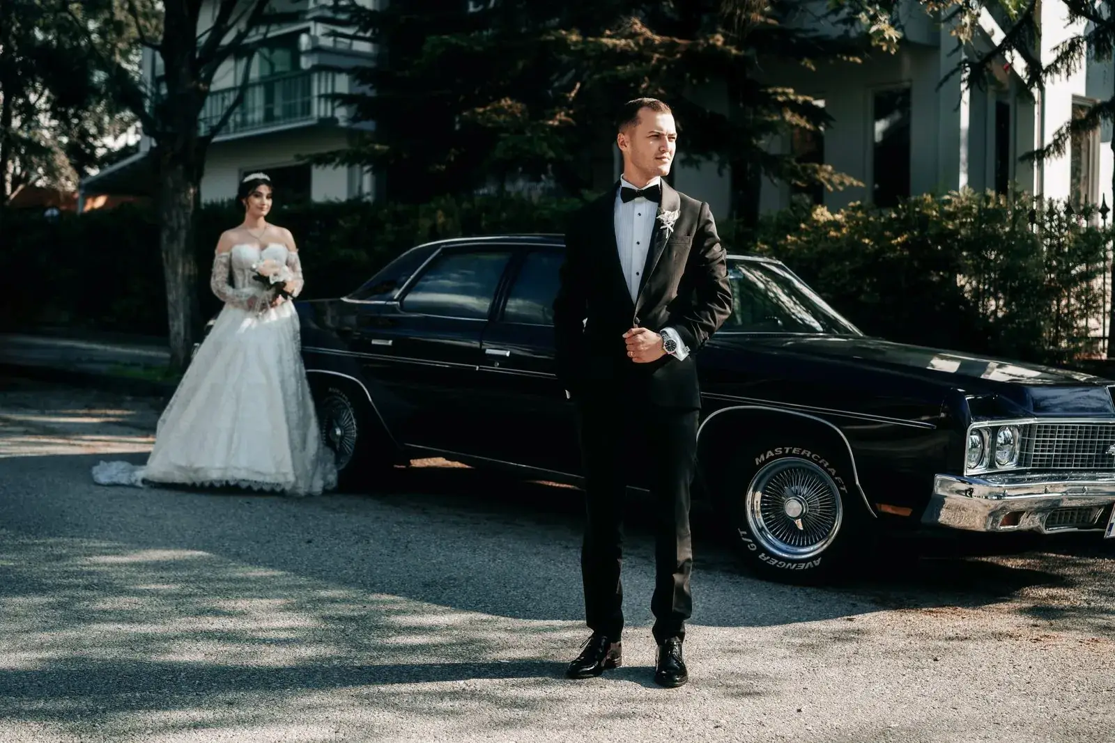 A bride and groom standing beside a black car
