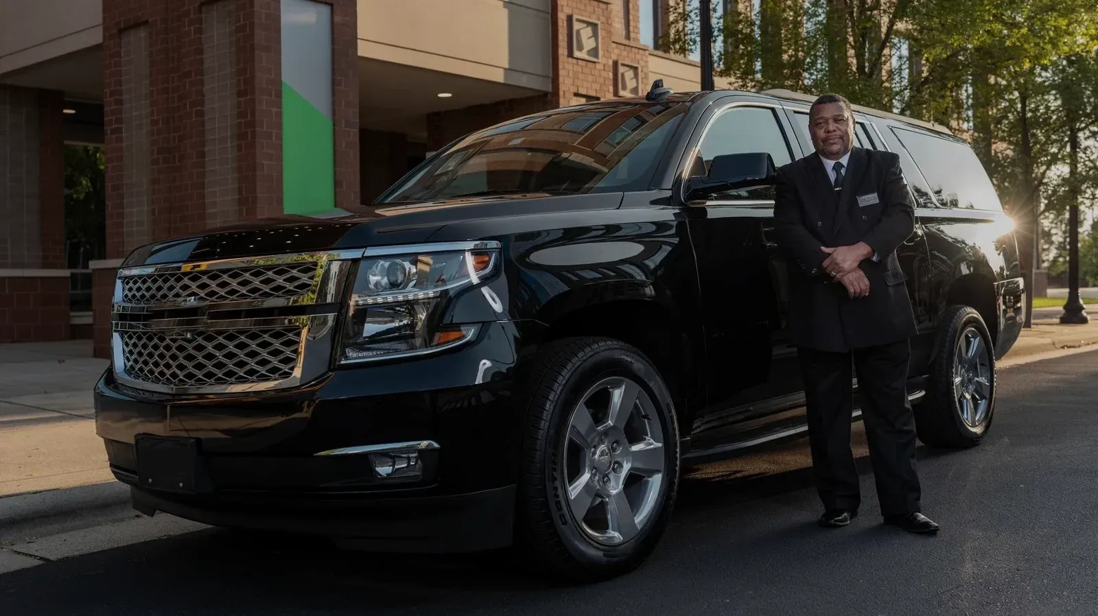 A chauffeur in a dark suit standing beside a black SUV