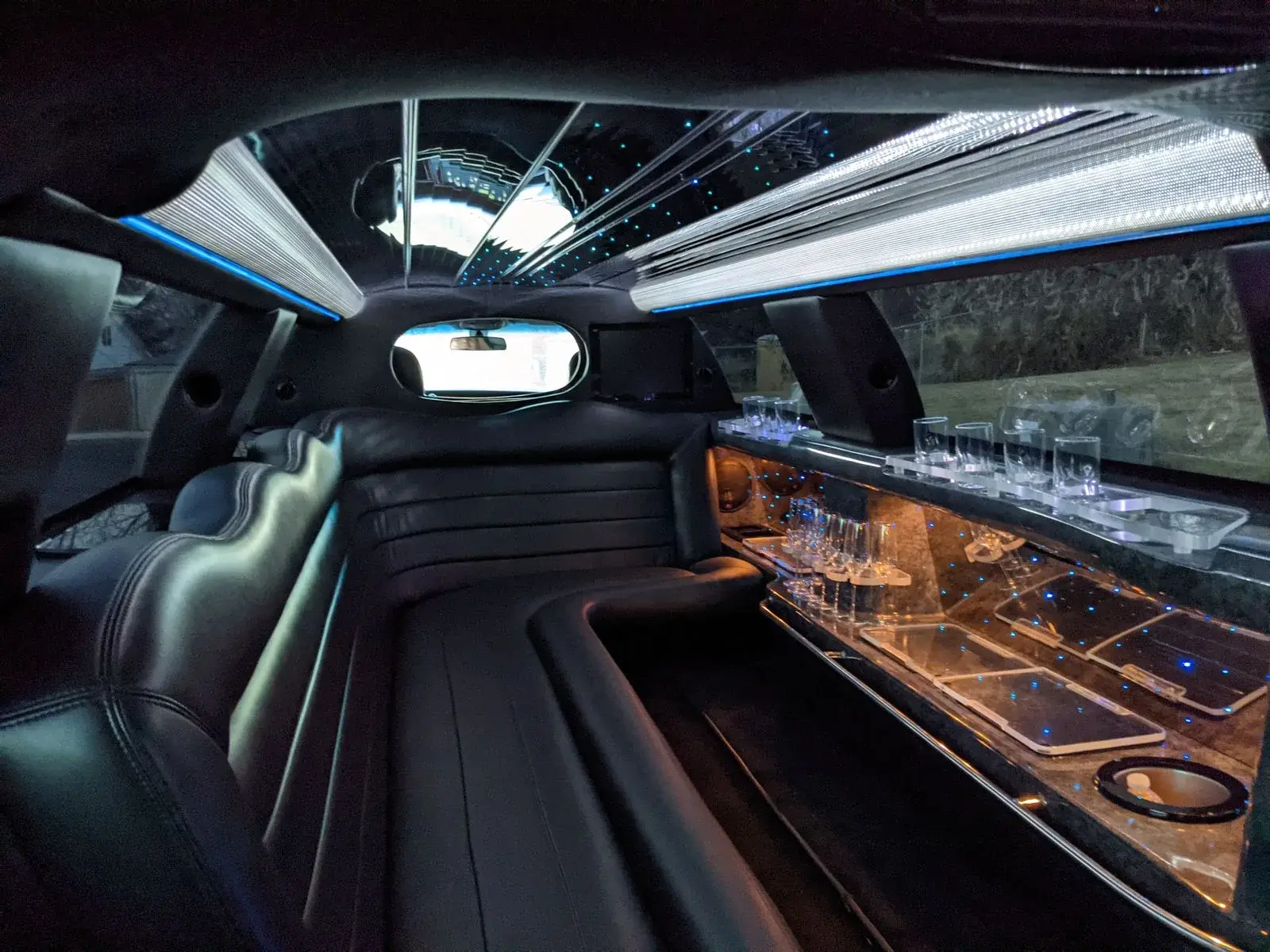 Leather bench seating, ambient lighting and a lit bar inside a luxury party vehicle