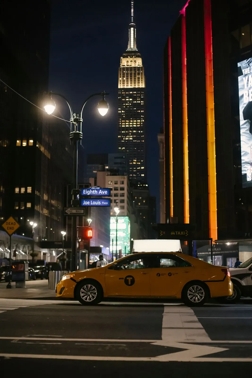 A Manhattan avenue at night with the Empire State Building lit